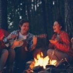 four friends enjoying music sitting around a campfire