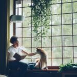 A girl petting her dog while reading a book.